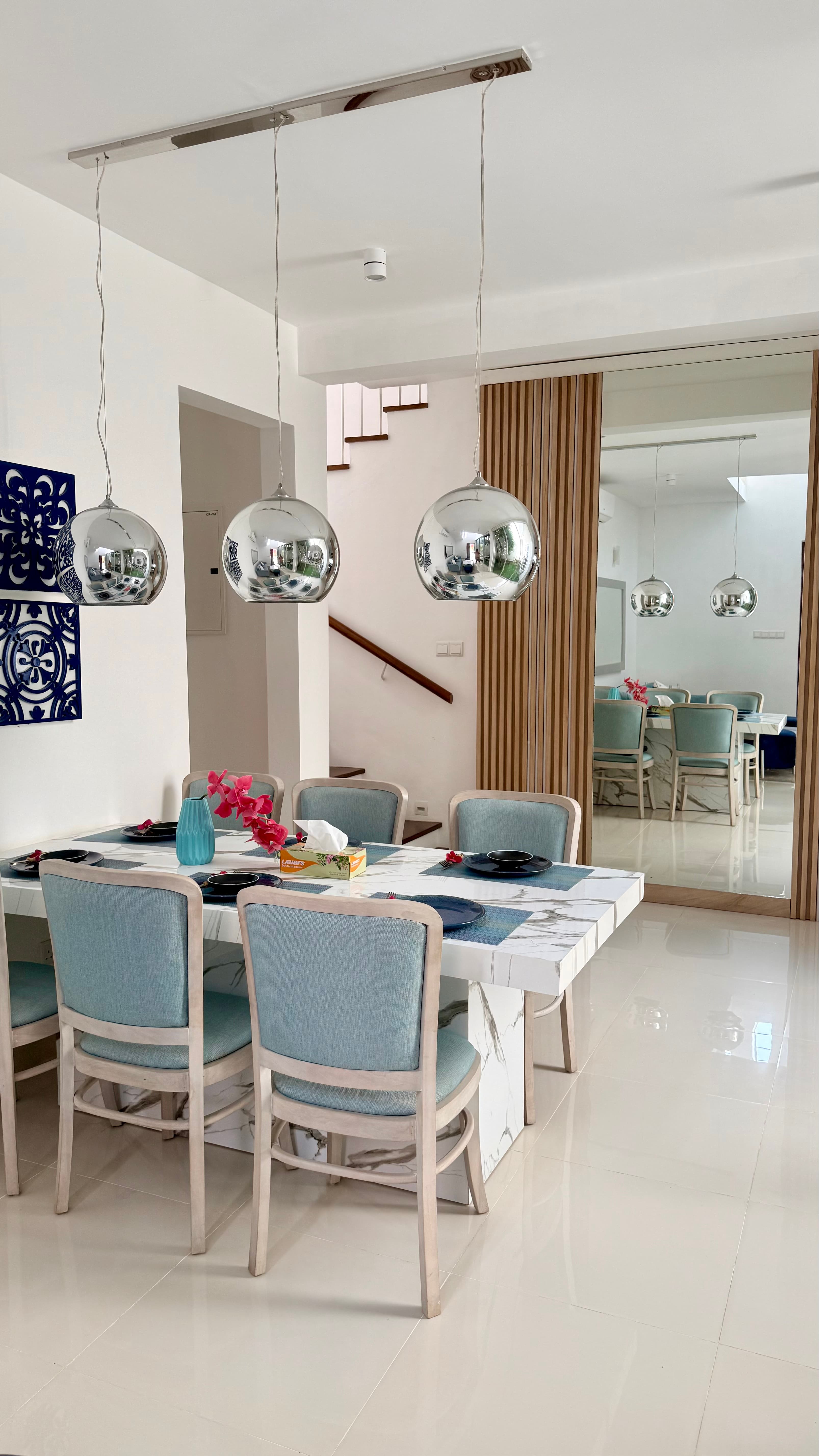 Villa 76 — formal dining room with marble table, teal upholstered chairs and chrome globe pendant lights